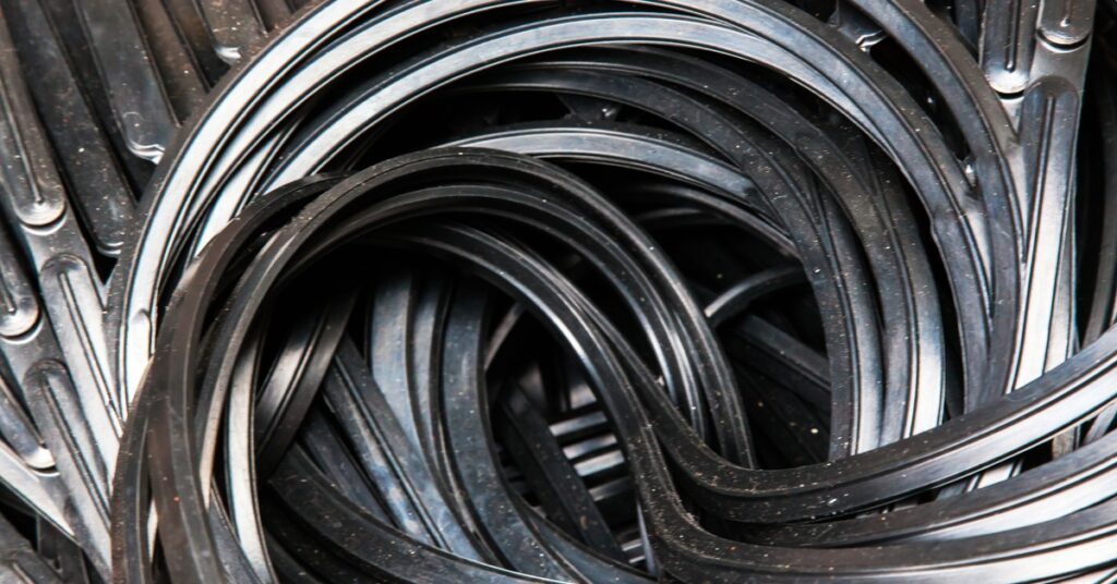 Multiple old and dusty black rubber gaskets piled and tangled together, placed over a black metallic surface.