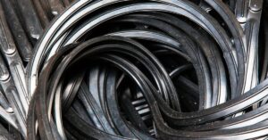 Multiple old and dusty black rubber gaskets piled and tangled together, placed over a black metallic surface.