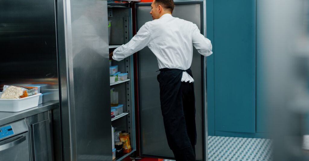 A kitchen worker looking for something inside a commercial refrigerator. The unit's door has black gaskets.