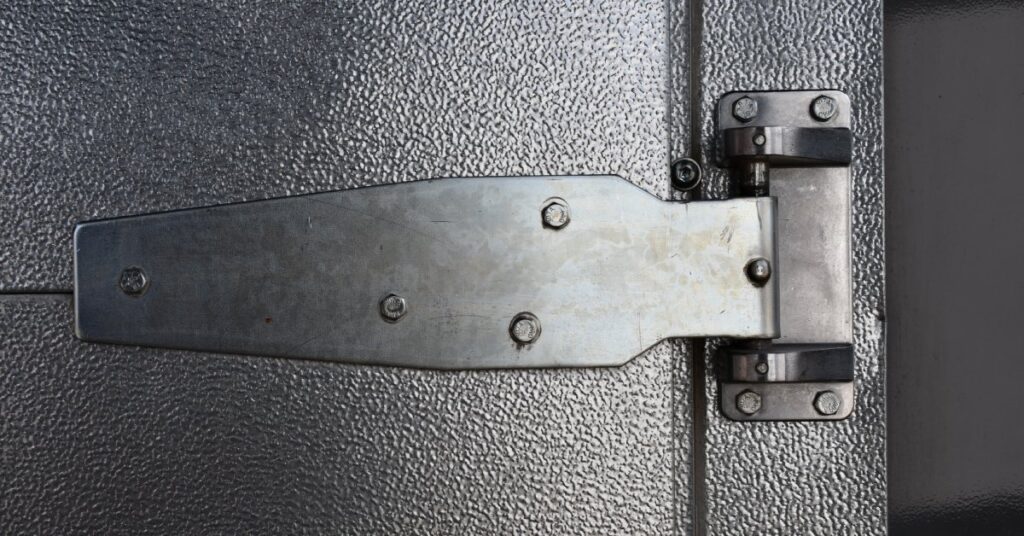 A close-up of a large metallic hinge on a refrigerator door. The hinge is black, shiny, and in good condition.