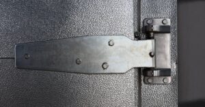 A close-up of a large metallic hinge on a refrigerator door. The hinge is black, shiny, and in good condition.