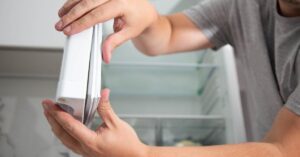 Close-up of the hands of a man firmly pressing with two hands on the white gaskets on a refrigerator door.