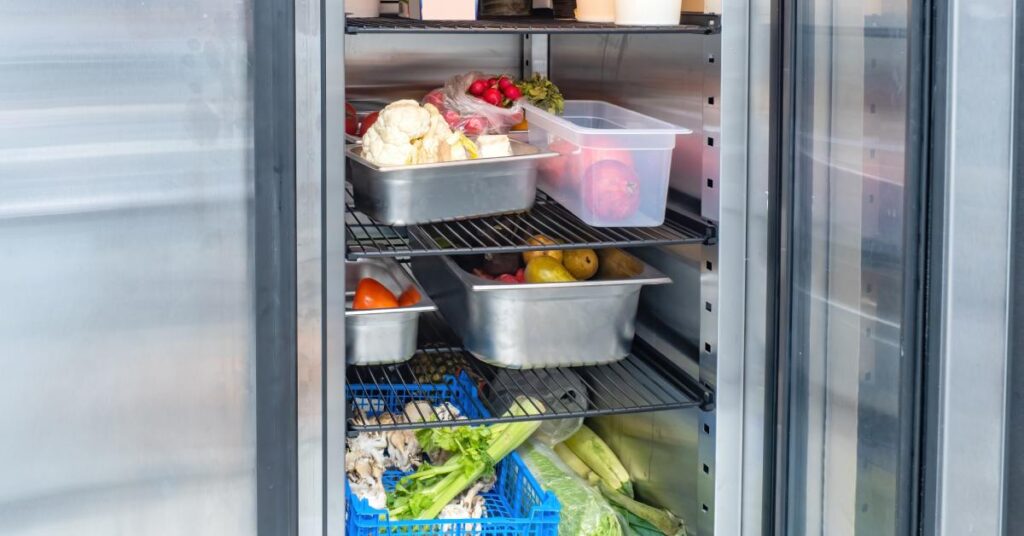 Close-up to the interior of a commercial refrigerator with an open door showing multiple racks with perishable food.