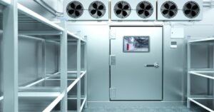The interior view of a walk-in freezer with multiple empty shelves, cooling fans, and a large door with a small window.