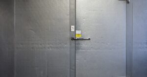 A close-up of a large freezer door, with two large metal hinges and two safety locks on the top and the side.