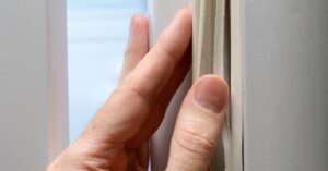 A close-up of a hand pulling on a white gasket, showing a torn edge attached to the side of a white door.
