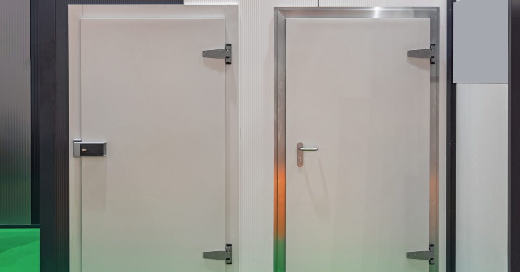 Two large white doors with metal hinges and large handles inside a room with white walls and a bright green floor.