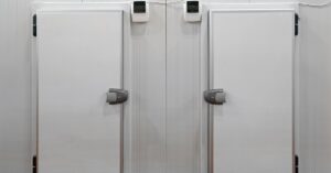 Two large white freezer doors with black hinges and large handles next to each other on a large white wall indoors.