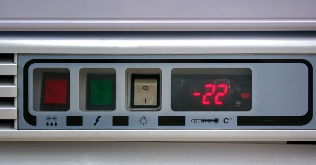 A close-up of a digital thermometer with a red, a green, and a white button next to a screen displaying the number -22.